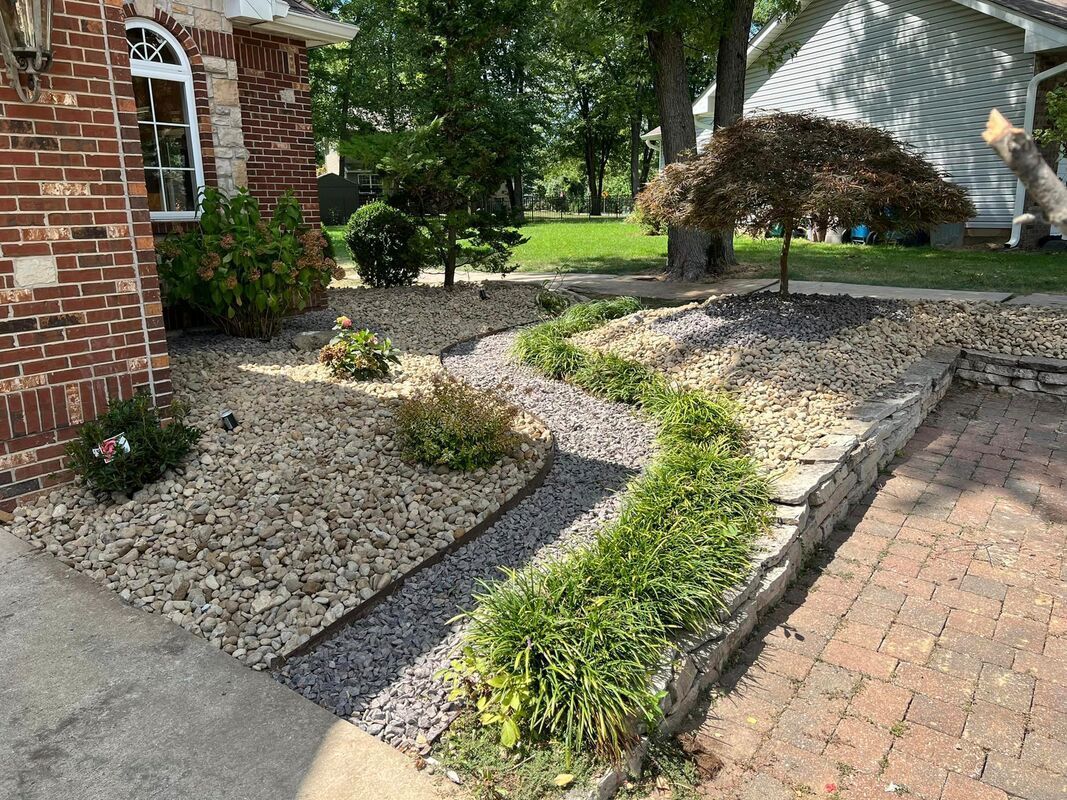 Front yard rock garden with small shrubs beside a brick house and brick walkway