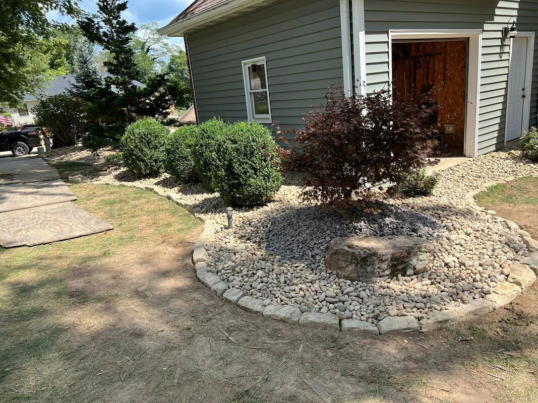 Front yard with stone landscaping, shrubs, and a gray house with a wooden door