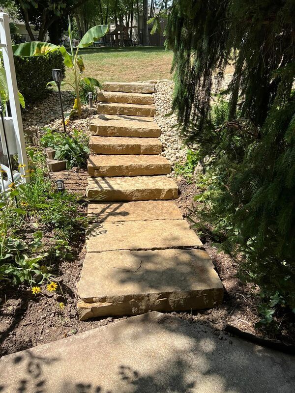 Stone garden steps leading up a grassy path, bordered by plants and shaded trees