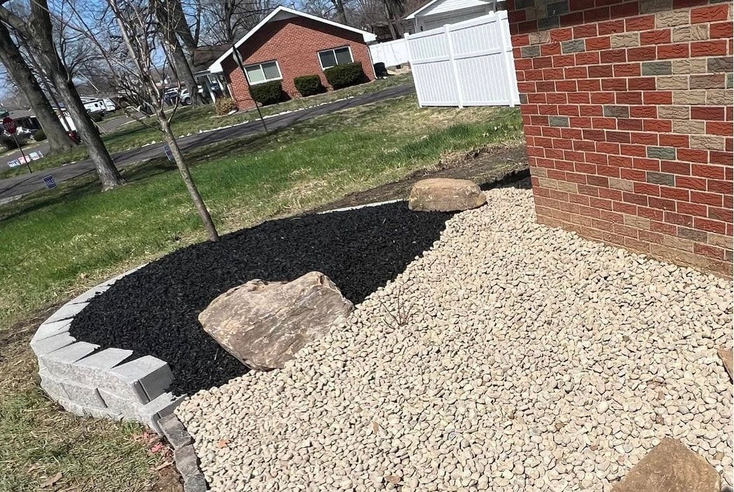 Curved gravel and black mulch bed beside a red brick house and white fence in a yard