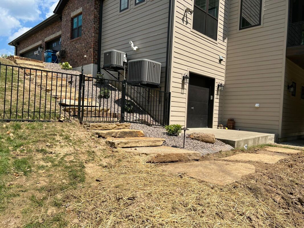 Backyard with a stone walkway, black railing, air-conditioning units, and a beige house exterior