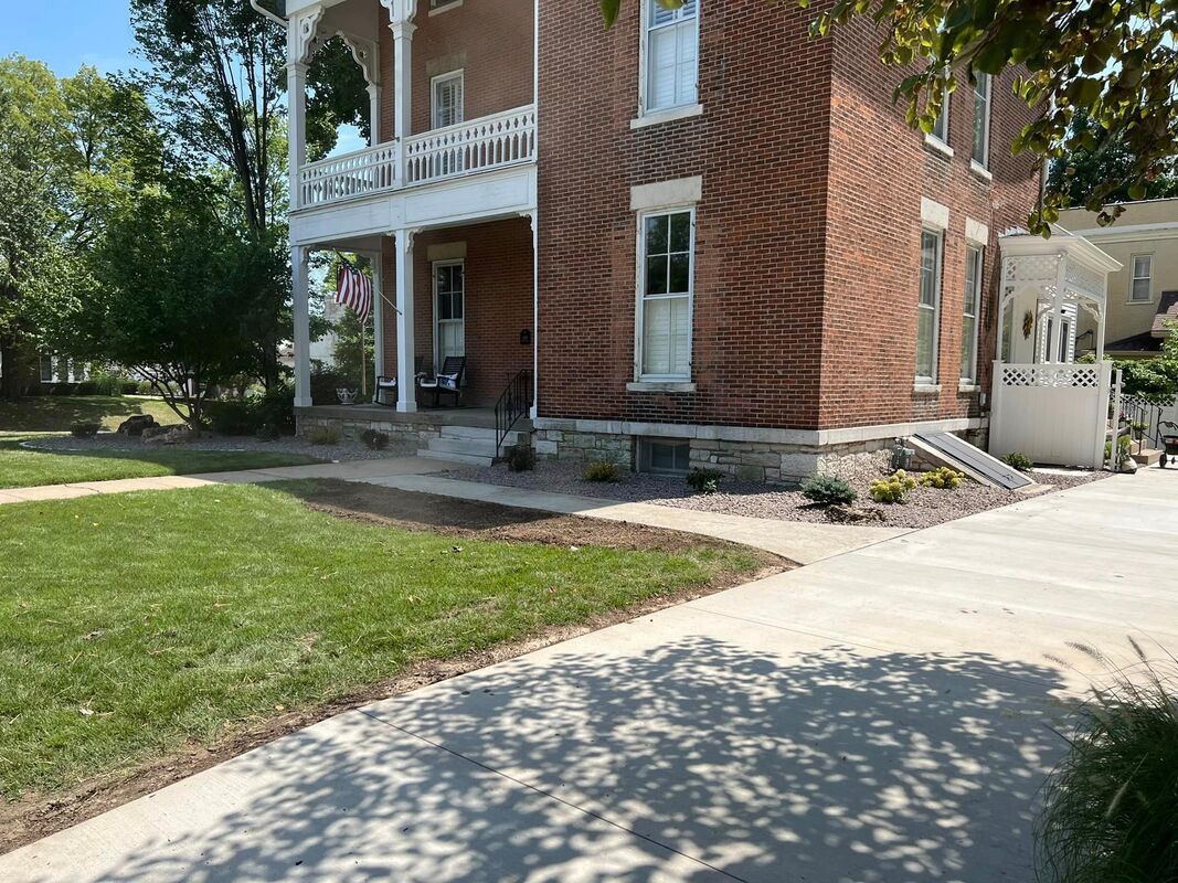 Brick house with white porch and balcony beside a sidewalk and green lawn on a sunny day