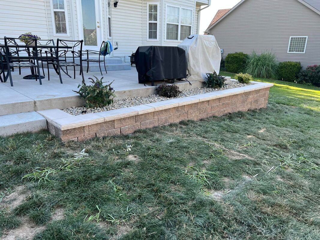 Back patio with a raised brick planter, grill under covers, and a grassy lawn beside the house.