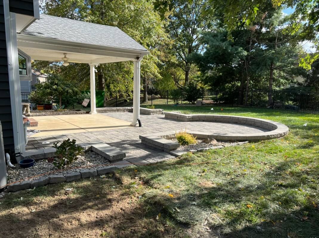 Backyard patio with a white gazebo, curved stone edging, and steps leading to a grassy yard.