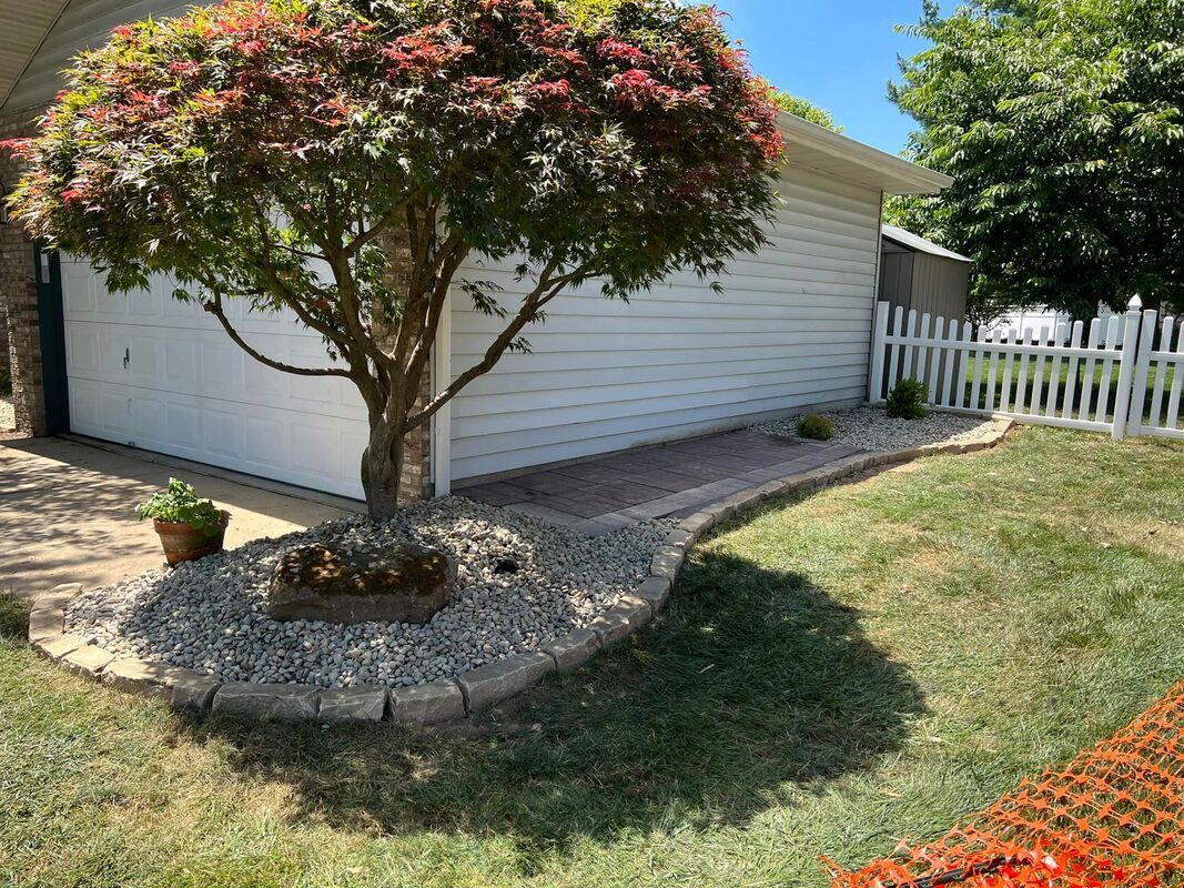 Backyard with a small tree in a rock bed beside a white garage and picket fence