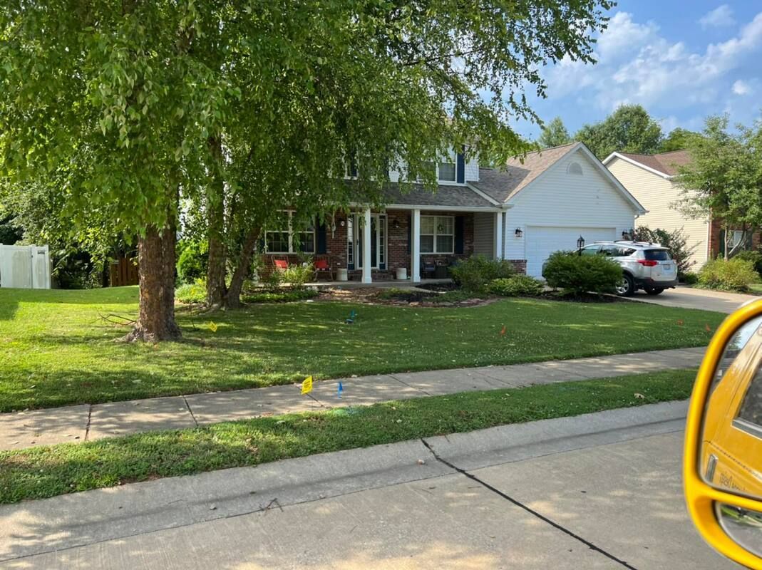 Suburban house with a large front yard, tree, sidewalk, and yellow car mirror at the edge of the frame