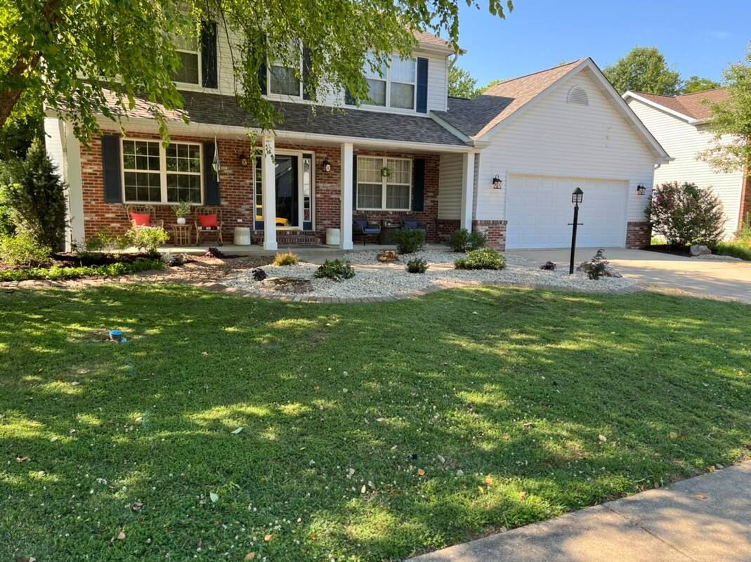 Suburban house with a front porch, white garage, and green lawn in daylight