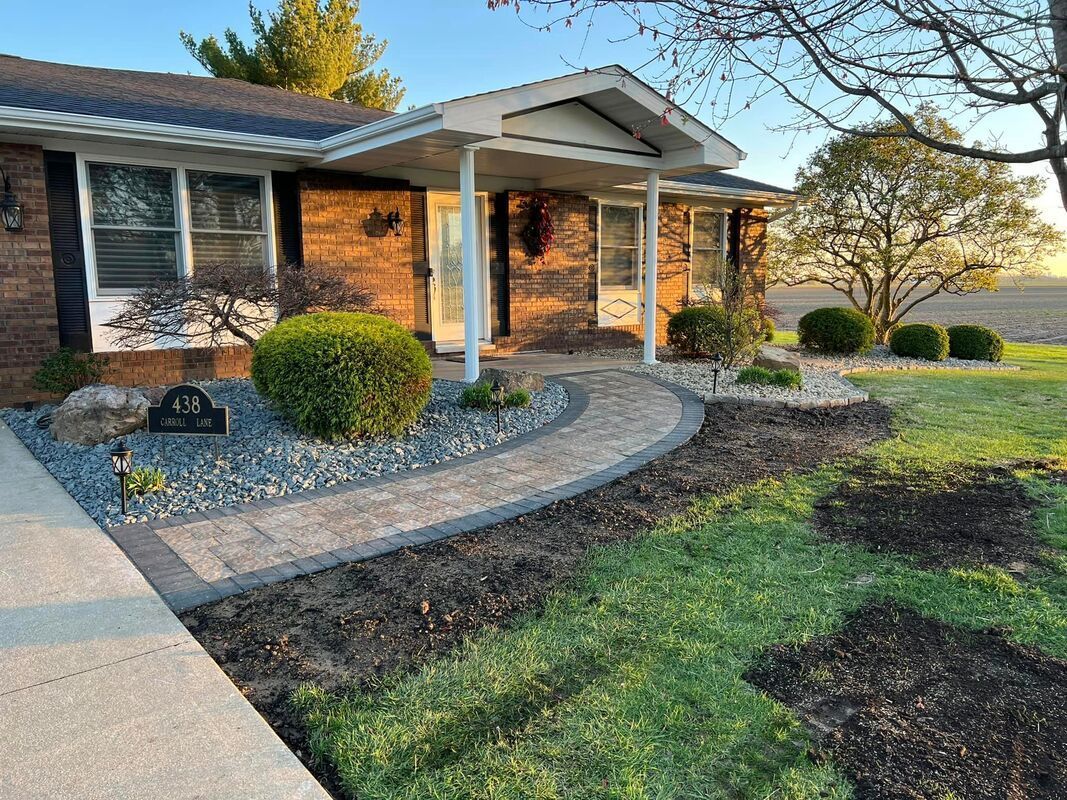 Brick house with a curved stone walkway, landscaped shrubs, and a front porch at sunset