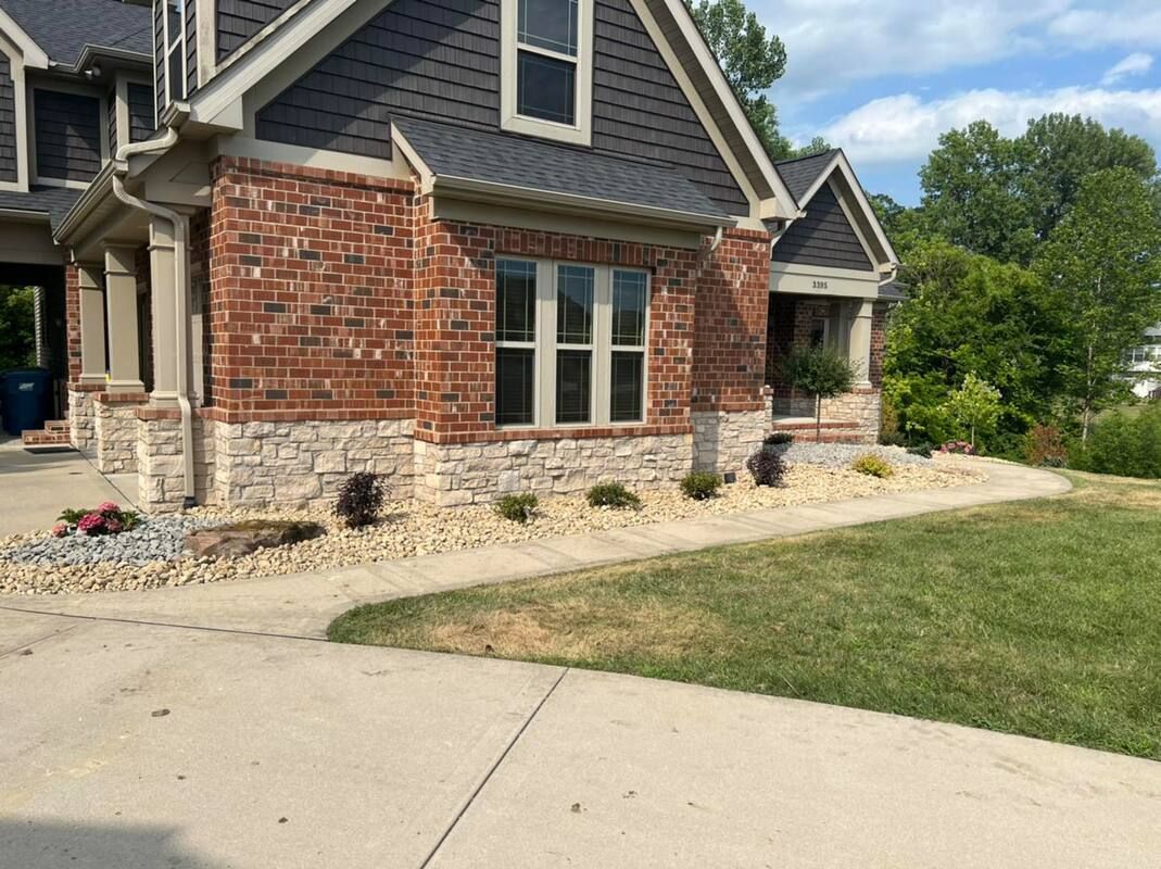 Brick house with gray shingle roof, front windows, and a curved concrete driveway in a suburban yard