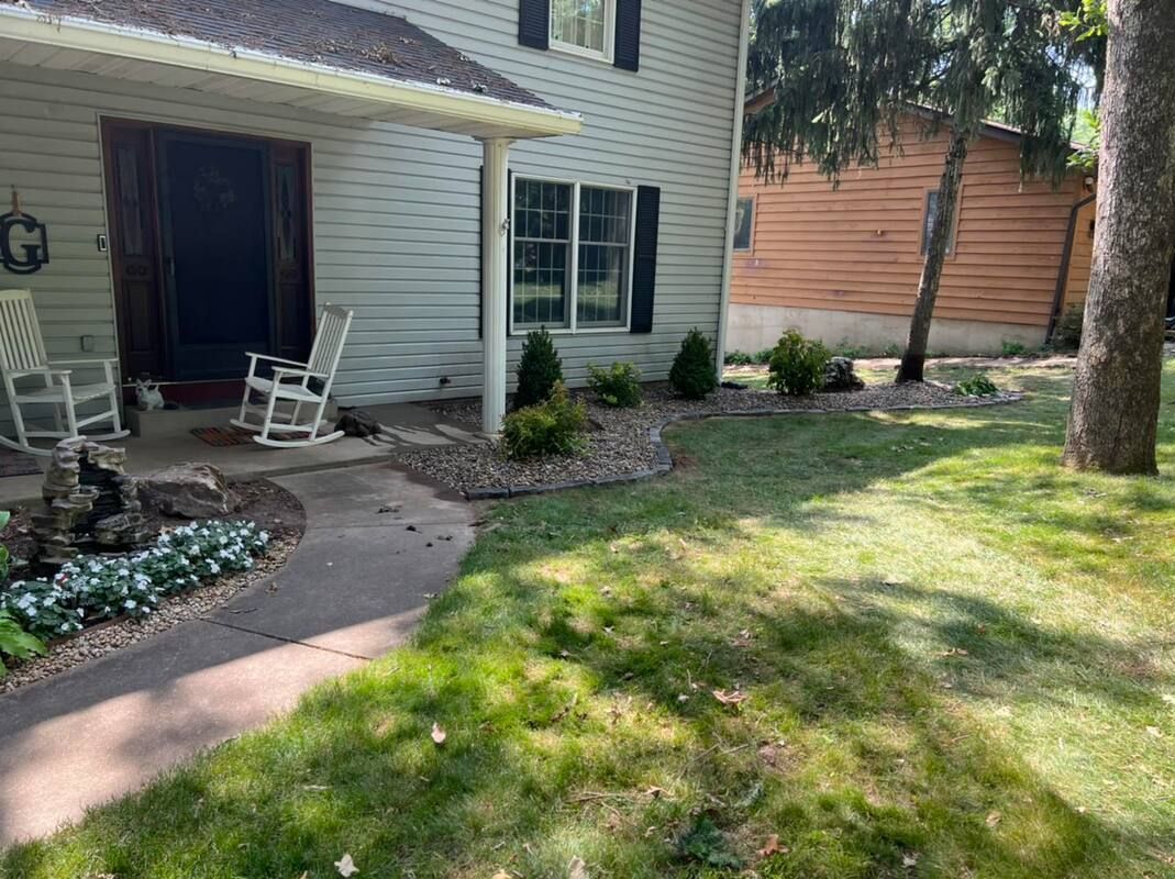 Suburban house exterior with front porch, stone walkway, and green lawn shaded by trees