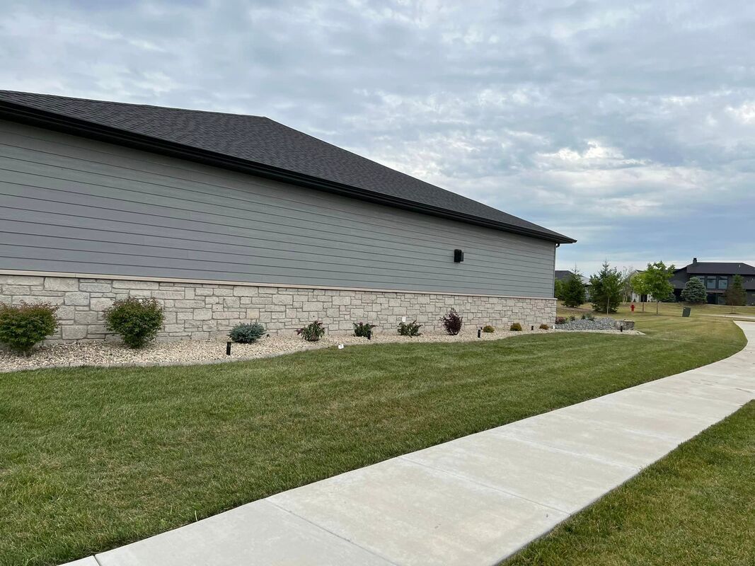Modern gray building beside a curved sidewalk and grassy lawn under a cloudy sky