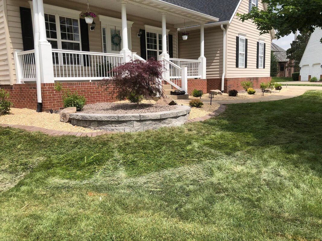 Suburban house with a front porch, white railing, stone landscaping, and a green lawn.
