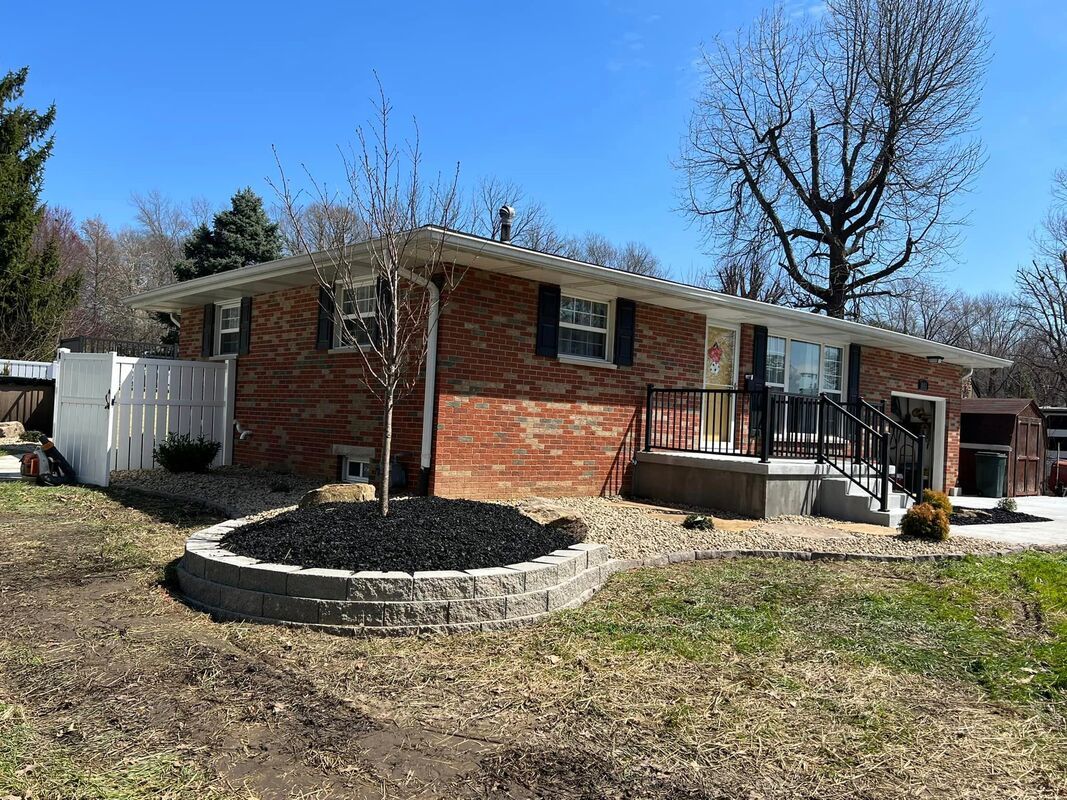 Brick ranch house with black shutters, a small front porch, and a circular stone planter in the yard