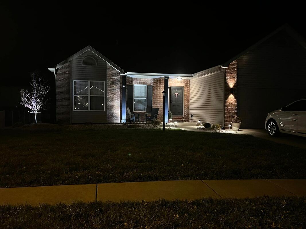 Single-story house at night, lit by porch lights, with a car parked at the right edge.