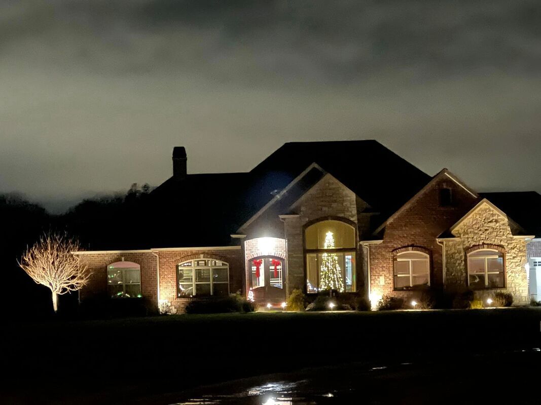 Large brick house at night, warmly lit windows and front entrance under a dark cloudy sky
