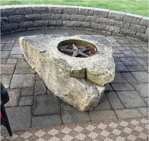 Large stone fire pit in a paved outdoor courtyard with a curved stone wall behind it.