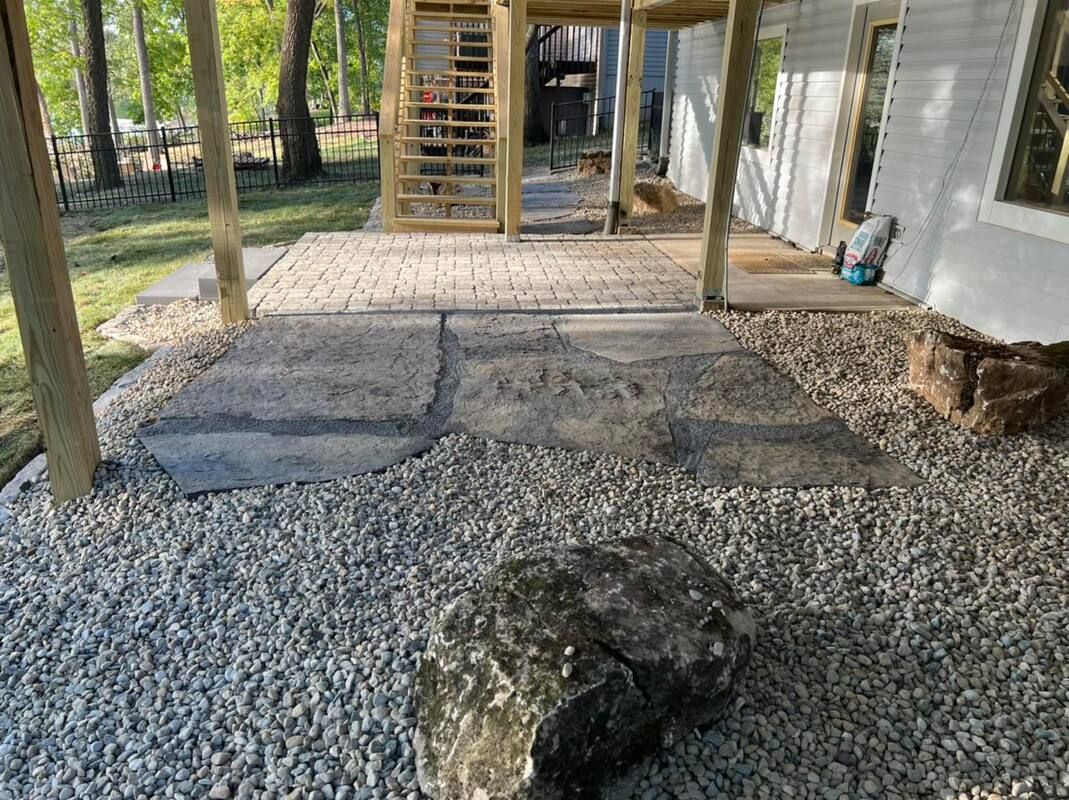 Gravel patio under a covered deck with concrete stepping stones and stairs beside a house