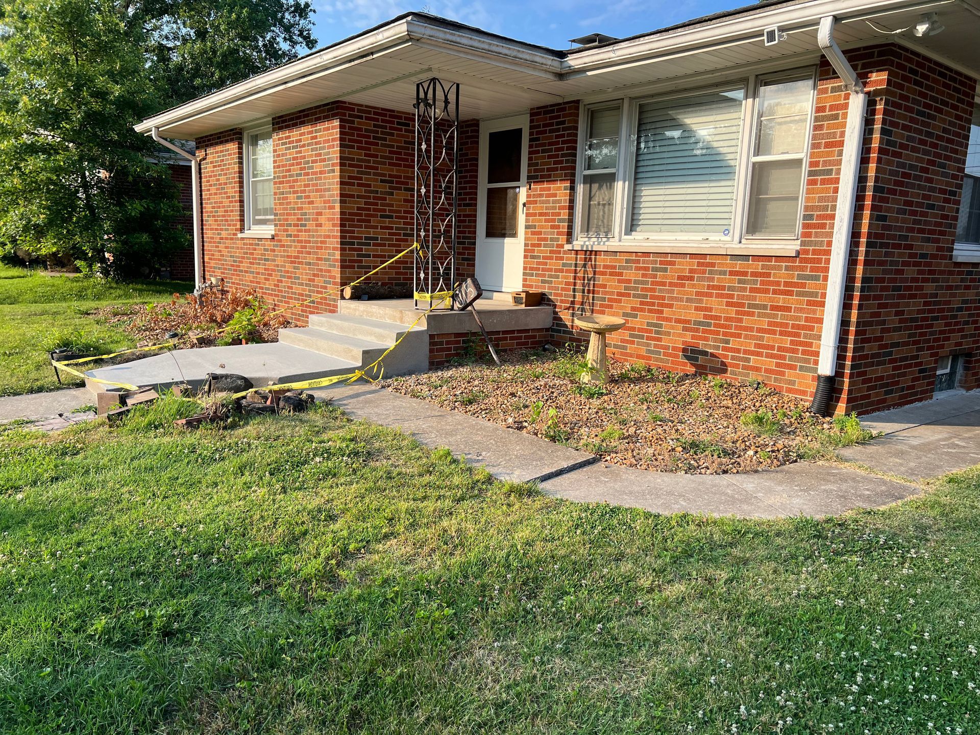 Single-story brick house with front porch, windows, and a small lawn in front.
