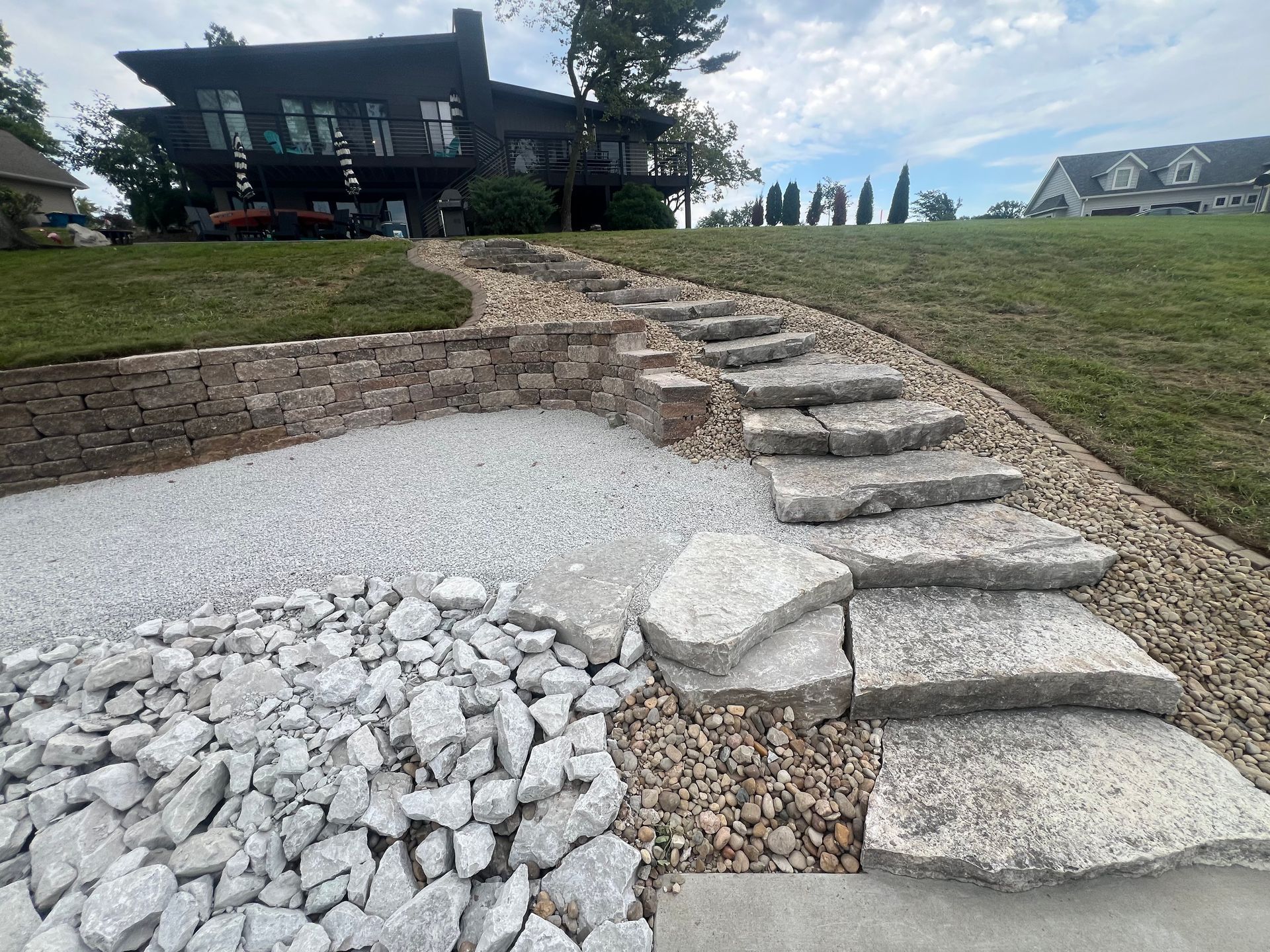 Stone steps in a sloped landscaped yard with gravel and a house in the background