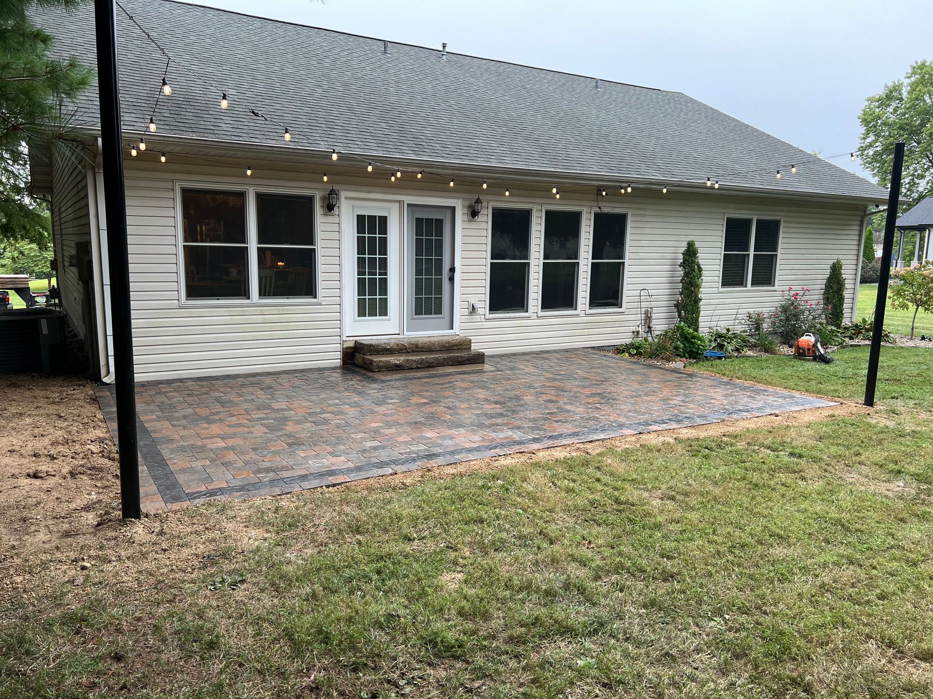 Single-story white house with a covered patio, brick paver area, and grassy yard