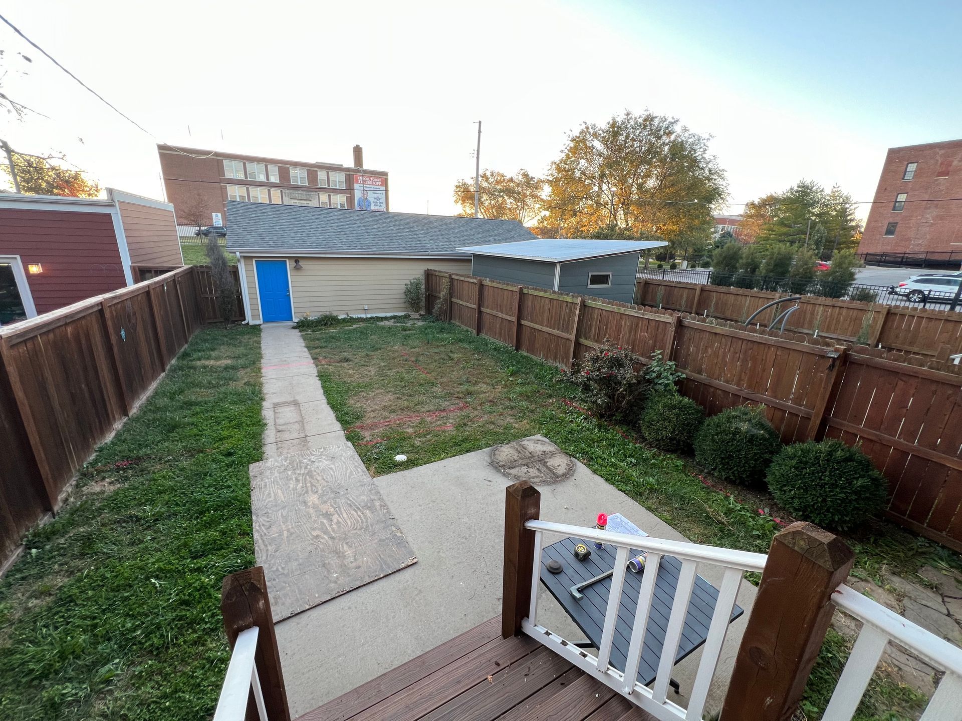 Backyard with concrete path, fenced lawn, and white gate leading to a blue shed at sunset