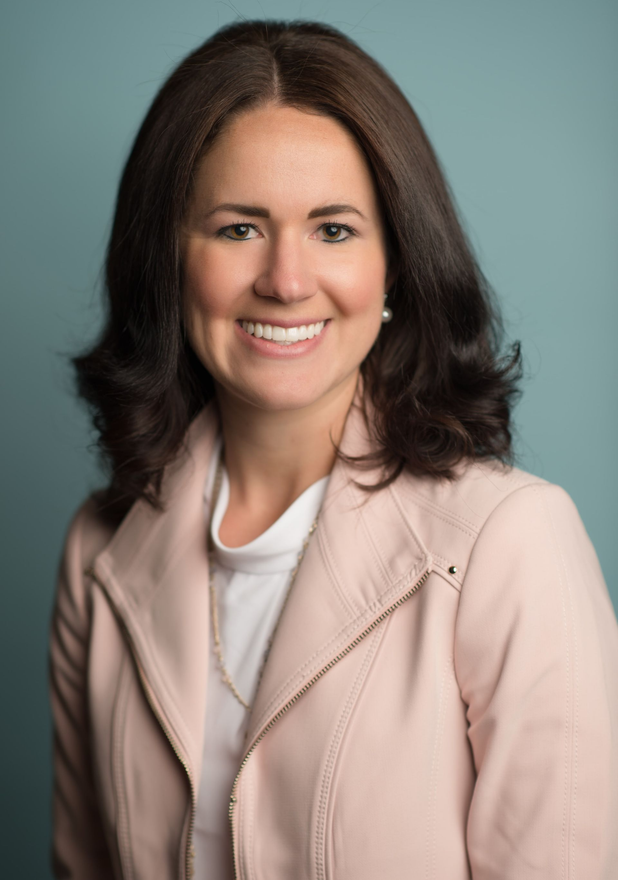 Studio portrait of a smiling woman in a light pink blazer against a gray background