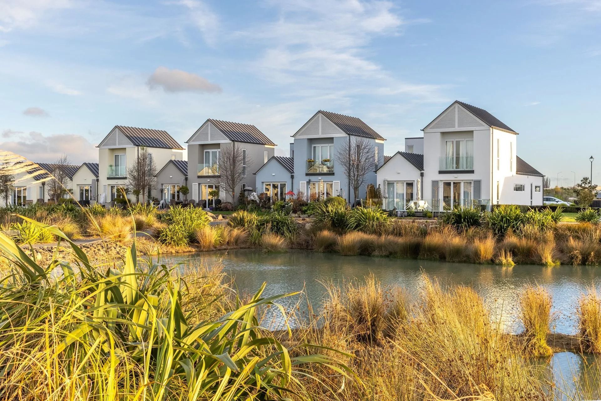 Row of modern houses with white and gray exteriors next to a pond with golden grasses.