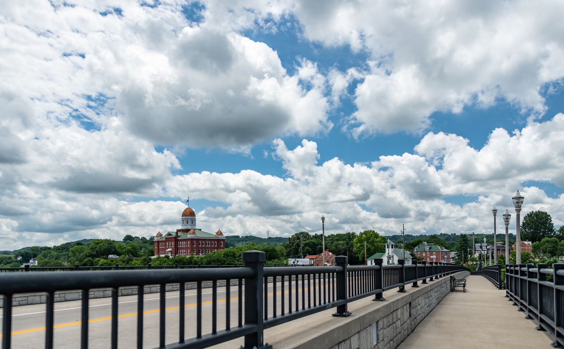 A walkway with a metal railing overlooks a road and a domed brick building under a cloudy sky.