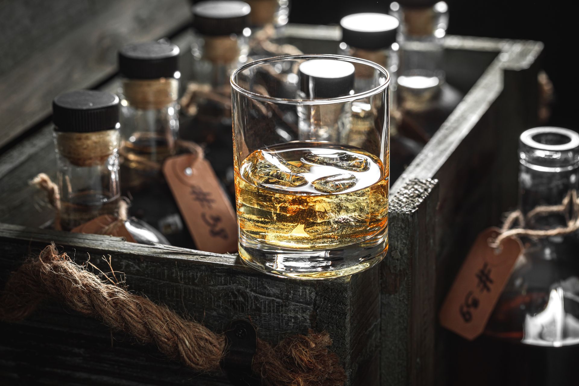 Glass of whiskey in a rustic wooden tray with small bottles in the background