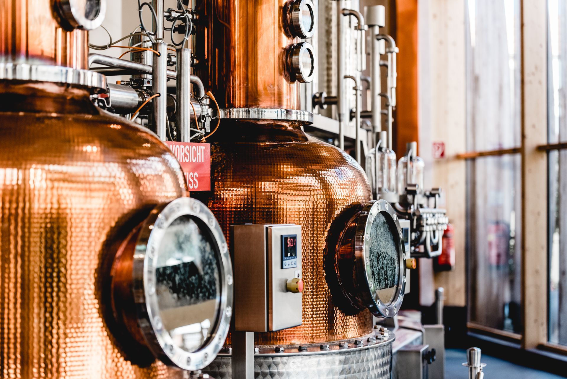 Copper distillery stills with glass windows and pipes inside an industrial facility