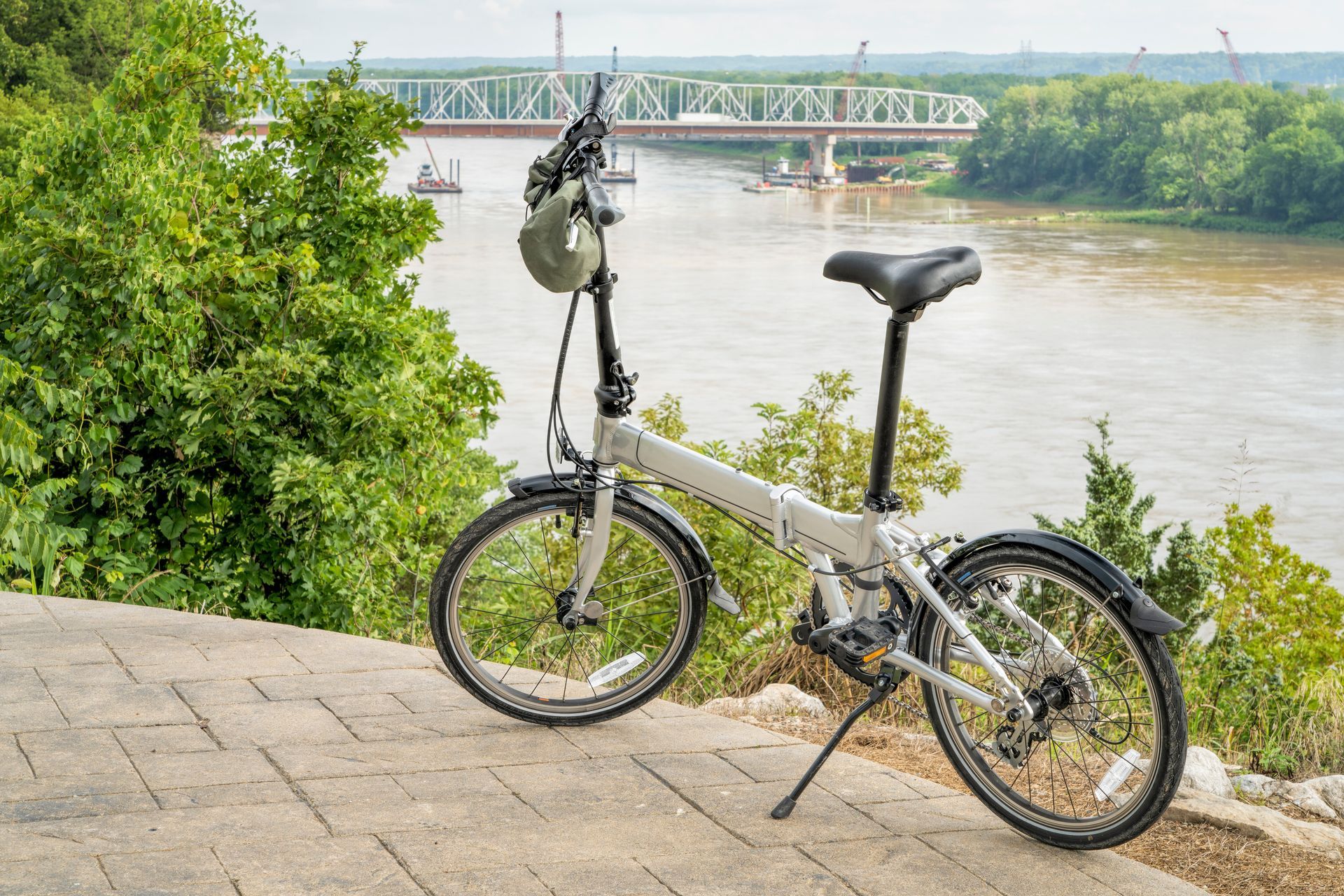 Bicycle parked on a riverside overlook with a bridge and trees in the background.