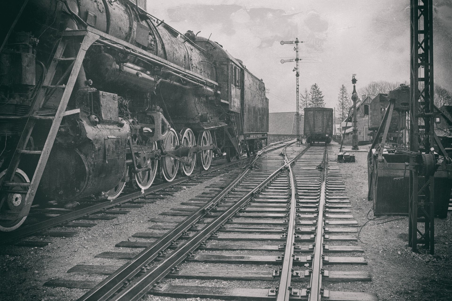 Steam locomotive on railroad tracks in a misty station yard, with freight cars and signal posts.