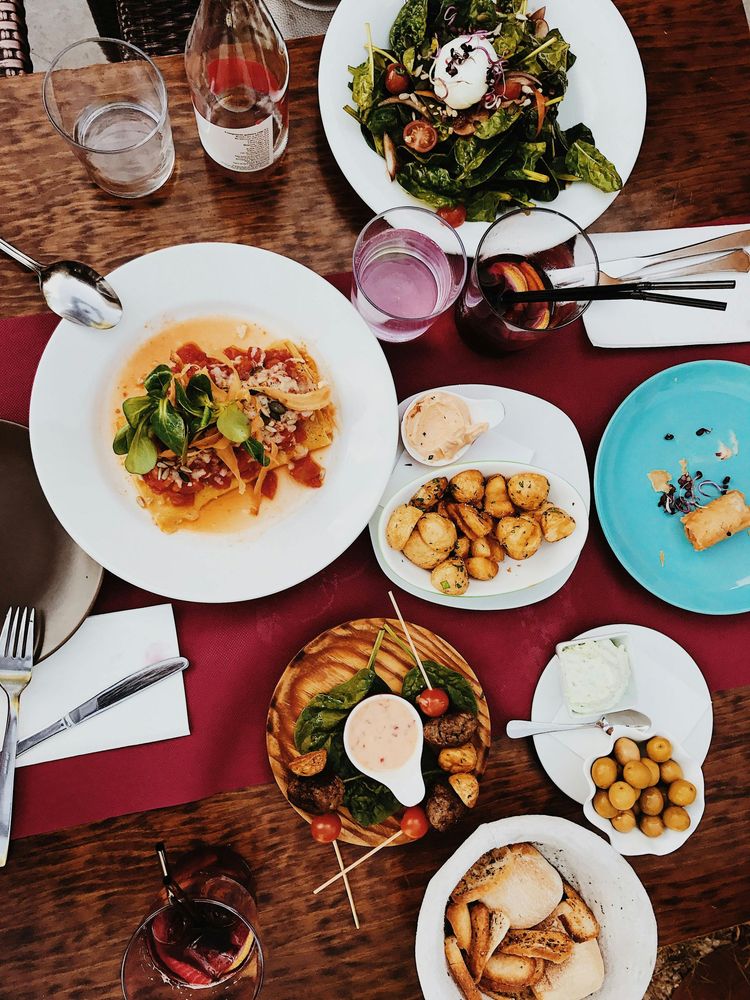 Overhead view of a dining table with various dishes, including salads, roasted potatoes, and appetizers on a red cloth.
