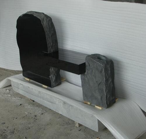 Black stone sculpture on a white pedestal, with an arch on one side and a block on the other connected by a dark bar.