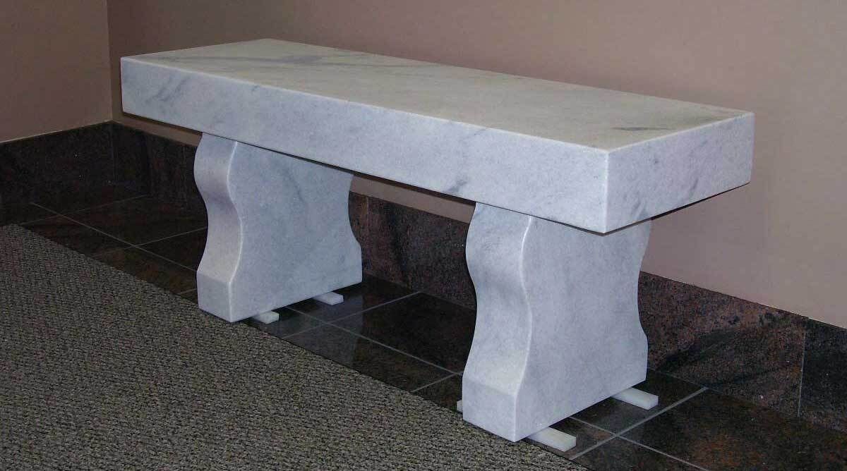 White stone bench with two curved legs on a tiled floor indoors