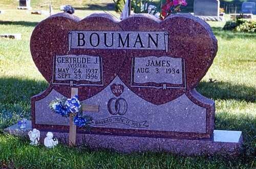 Marble gravestone with engraved names and blue flowers in a grassy cemetery.