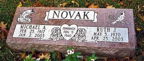 Novak family gravestone with engraved portraits and names, set among flowers and grass
