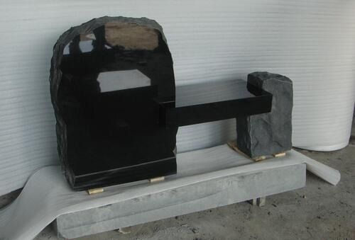 Black mailbox mounted on a wooden post and concrete base outdoors, with a white wall behind it