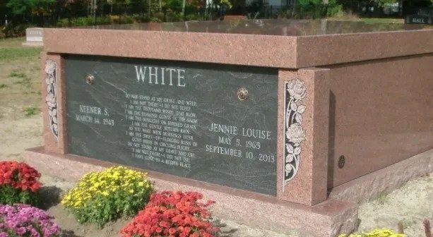 Bronze memorial wall plaque with engraved names and flowers in front outdoors