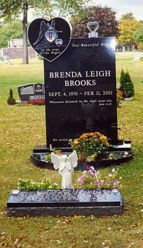 Black gravestone with white flowers and heart plaques in a grassy cemetery.