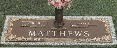 Bronze Matthews gravestone with flowers in a cemetery, bearing the names John and Mary