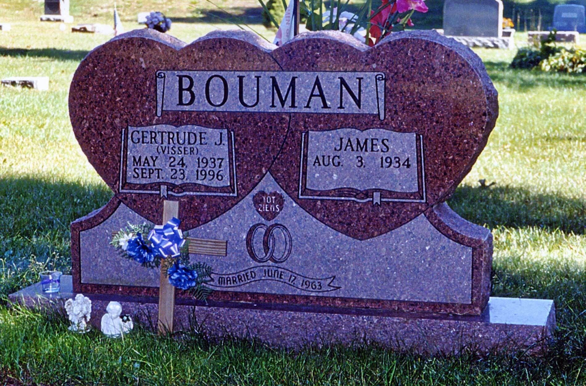 Bouman gravestone in a cemetery, with engraved names and dates, decorated with blue flowers.