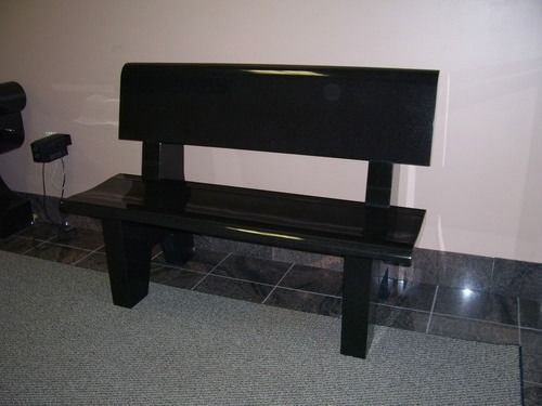 Black wooden bench against a wall on a tiled floor in a hallway or lobby.