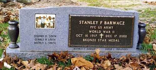 Two engraved memorial plaques on a gray stone bench amid fallen leaves outdoors.