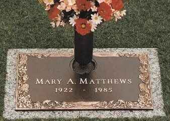 Gravestone for Mary A. Matthews, 1922–1985, with flowers in a vase on a grassy lawn.