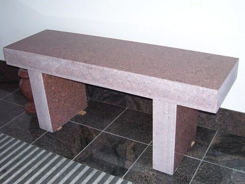 Stone bench with a rectangular seat and two thick legs on a tiled floor.