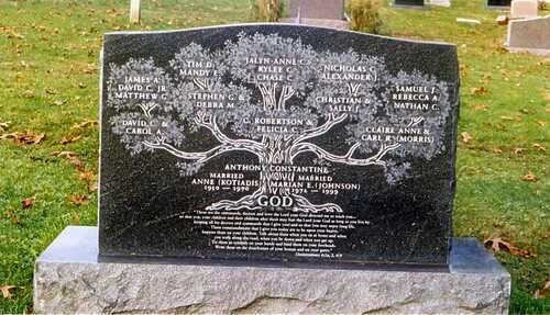 Black memorial headstone with engraved tree and text, set on a stone base in a grassy cemetery.