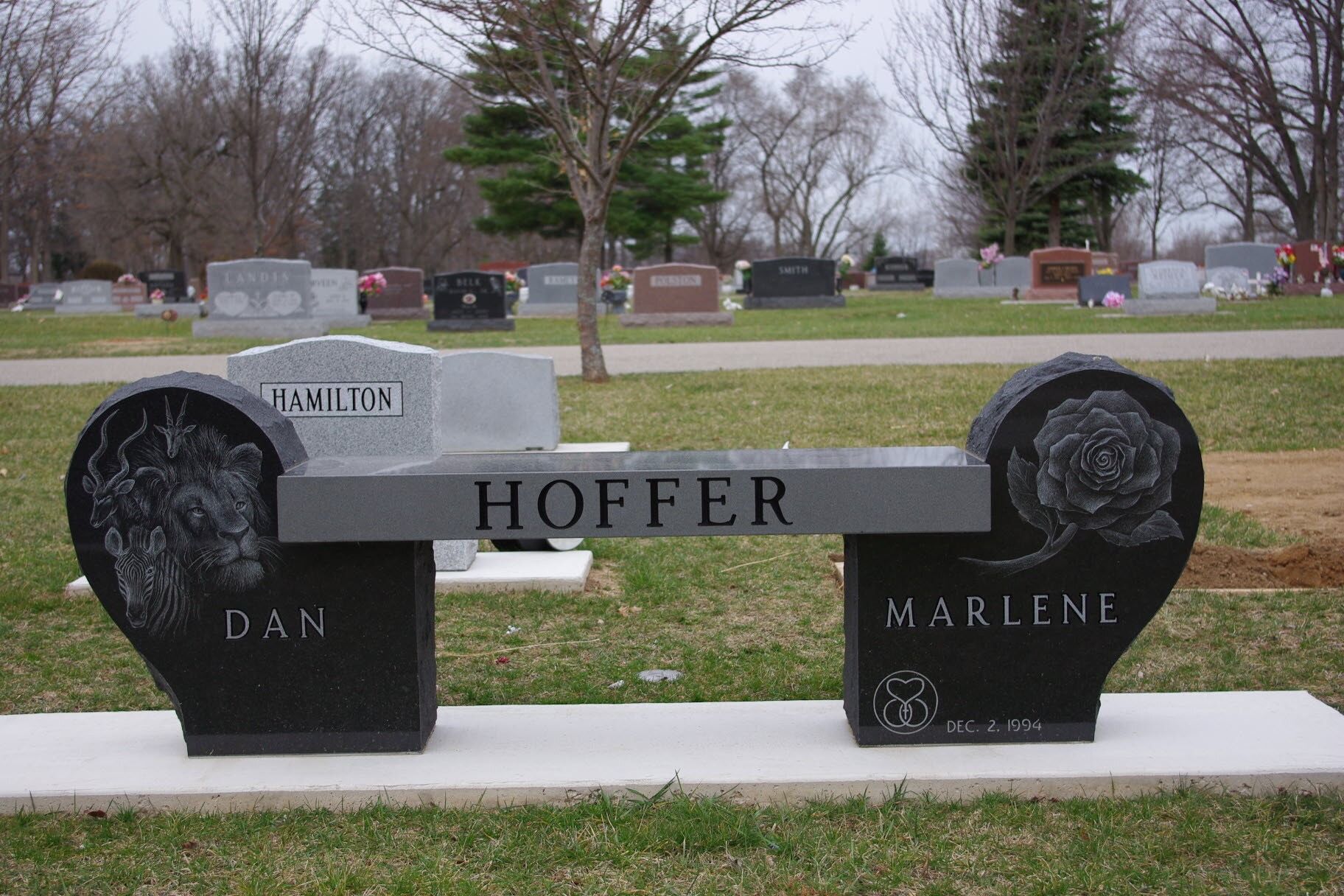 Black and gray memorial bench with names Hoffer, Dan, and Marlene in a cemetery park