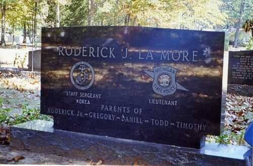 Granite memorial plaque for Roderick J. LaMore in a wooded cemetery, with military emblems and engraved names