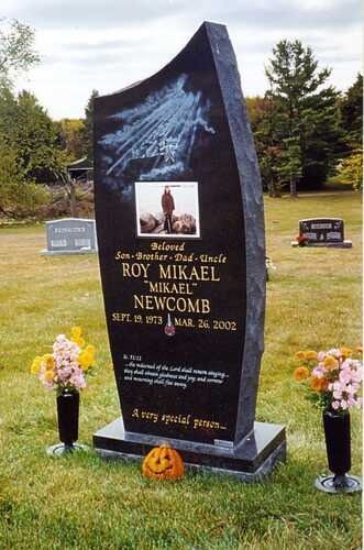 Black memorial headstone with flowers and small lanterns in a cemetery lawn.